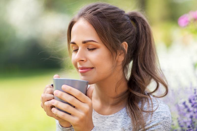 Frau draußen mit Teetasse in der Hand, riecht genüsslich - Sympbolbild für Hausmittel bei Reizdarm und Verdauungsbeschwerden