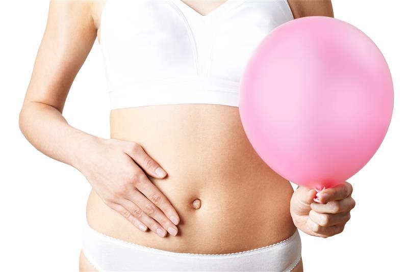Frau hält sich mit der einen Hand den Bauch und mit der anderen einen Luftballon - Symbolbild für Behandlungsmöglichkeiten bei Blähungen und Völlegefühl: Digestopret