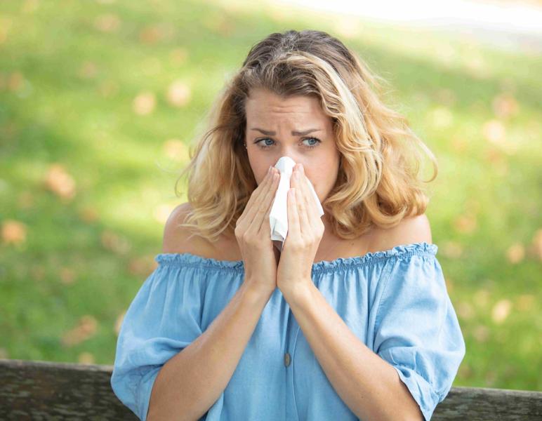 Blonde Frau auf einer Bank im Park beim Naseputzen