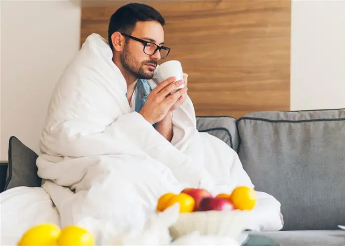 Mann umwickelt mit einer Decke und einer Tasse in der Hand