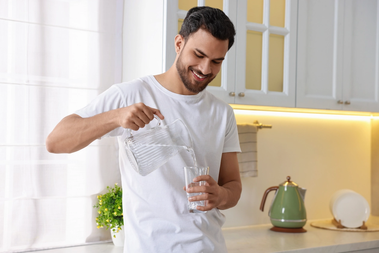 Mann, welcher sich ein Glas Wasser einschenkt