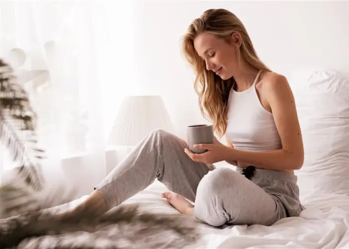 Frau sitzt mit Tasse auf dem Bett